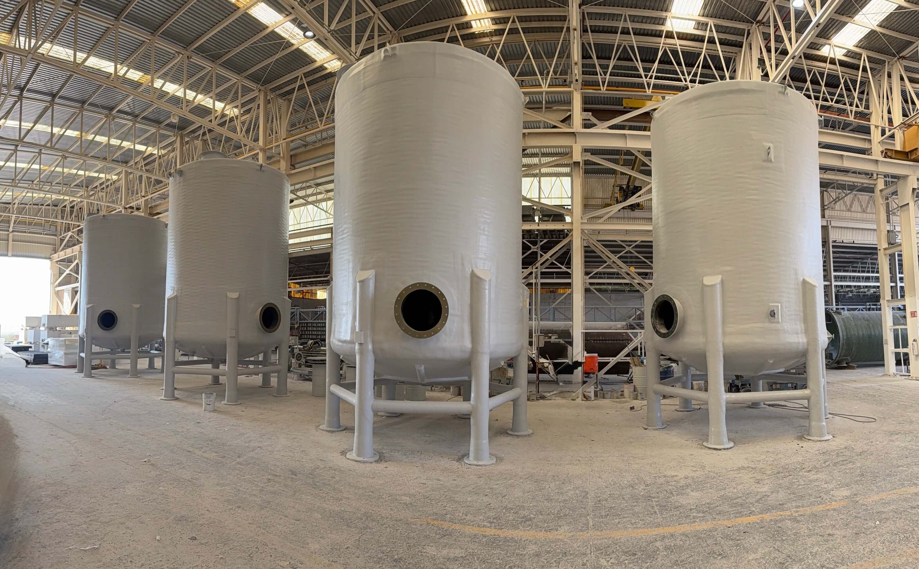 White FRP corrosion-resistant storage tanks for aggressive chemical service, staged in a fiberglass fabrication shop