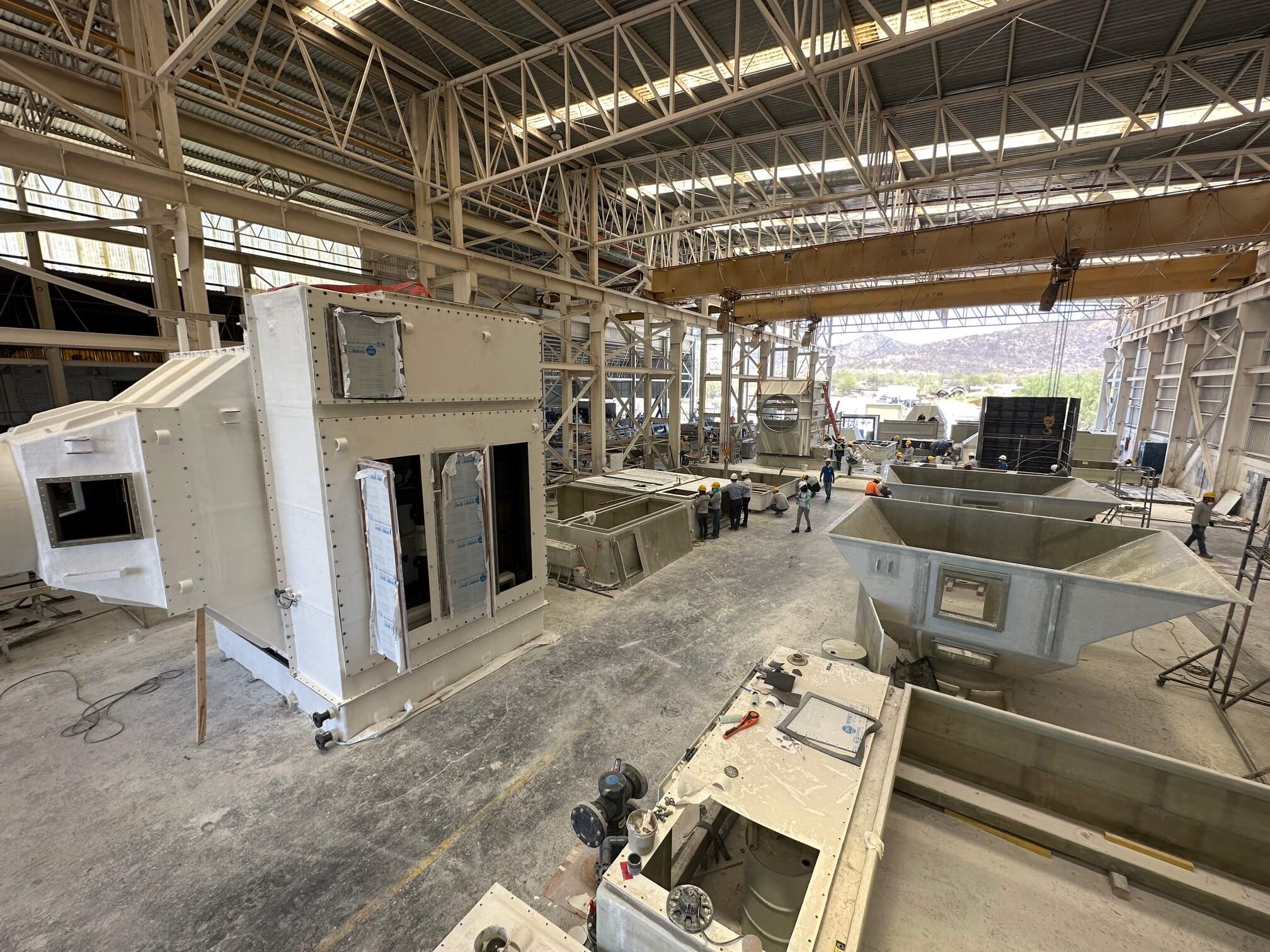 FRP scrubber ductwork and fabricated hoppers staged on the shop floor at Plastimarmol's manufacturing facility, with overhead crane and workers in the background