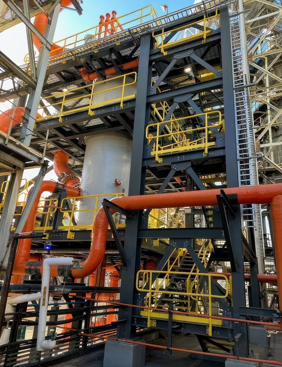Large-diameter FRP piping with flanged joints and 90-degree elbows routed through a steel support structure at an industrial plant